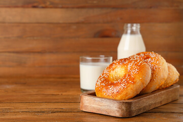 Board with tasty bagels and glass of milk on wooden background