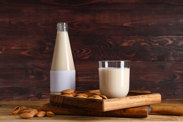 Glass and bottle of fresh almond milk with nuts on wooden background