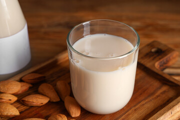 Glass of fresh almond milk and board with nuts on wooden background