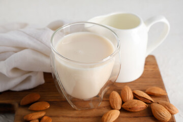 Glass and jug of fresh almond milk with nuts on white background