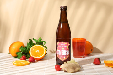 Bottle of tasty kombucha tea with orange, ginger and strawberry on beige tile table