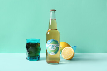 Bottle and glass of tasty kombucha tea with lemon on turquoise background