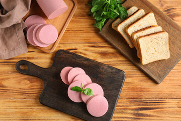 Boards with slices of tasty boiled sausage, bread and basil on brown wooden background