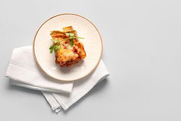 Plate with piece of tasty enchilada and napkin on light background