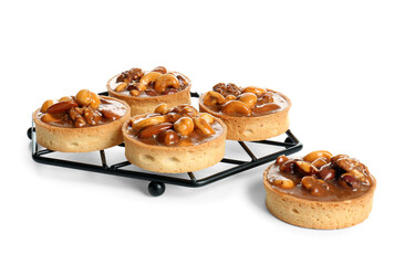 Tasty tarts with nuts and caramel on stand against white background