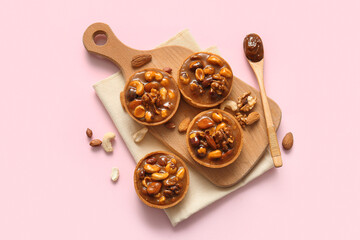 Tasty tarts with nuts and caramel on wooden board against pink background
