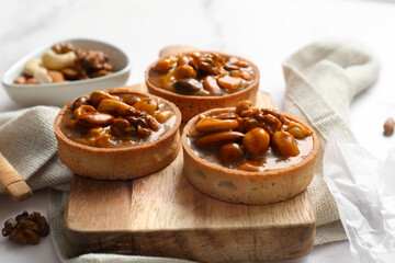 Tasty tarts with different nuts and caramel on wooden board against grunge white background