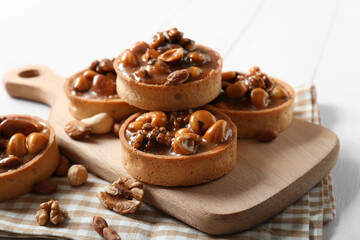 Tasty tarts with different nuts and caramel on board against white wooden background