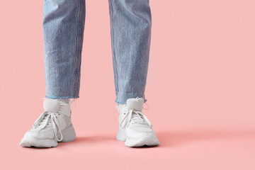 Female legs in stylish white sneakers and jeans on pink background