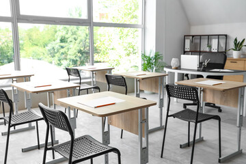 Desks with papers and chairs in empty classroom at school
