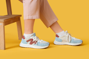 Female legs in sneakers with stool on yellow background