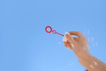 Female hand with soap bubble wand on blue sky background