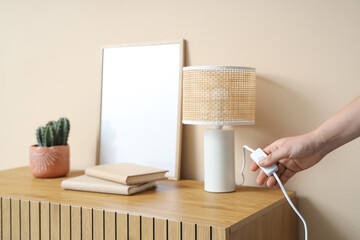 Woman turning on desk lamp on wooden cabinet near beige wall