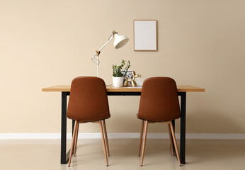 Wooden table with houseplant, figurine, magazines and desk lamp near beige wall