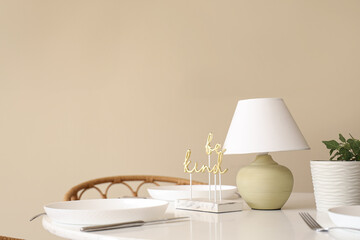 Served dining table with crockery, houseplant and desk lamp near beige wall