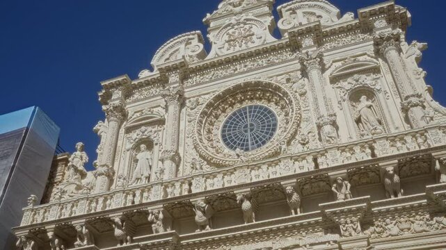 Baroque architecture of the basilica di santa croce in lecce, puglia, italy, featuring intricate stone carvings and sculptures against a bright blue sky.