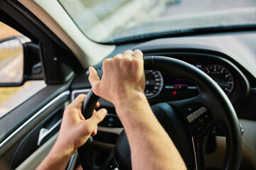 Man driving a car with hands on the steering wheel, focusing on the road ahead, interior view showcasing dashboard details and blurred scenery in the background