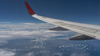 Obraz premium An airplane wing on a blue sky background. Close-up. Below is the ocean, white clouds. Malaysia.