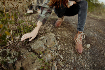 A woman on a rural journey, stylishly picking wild plants in her checked shirt and boots