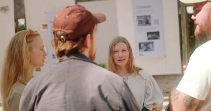 A group of friends stands at an outdoor contemporary art exhibition and engage in a dialogue. Discussion between people about creativity. Friends share their impressions. Spending time together.