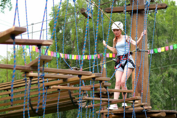 a woman in a helmet and belay goes through obstacles on a rope course in the park