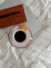 Cup of coffee, cookies, laptop, notebook on the bed top view