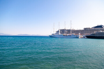Large cruise ships and a sailboat are docked at the pier against the blue sea on a clear summer...