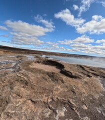 A vivid geothermal landscape in Iceland featuring rugged terrain and a bright, cloud-filled sky. The scene captures the unique beauty of Iceland's natural geothermal wonders.