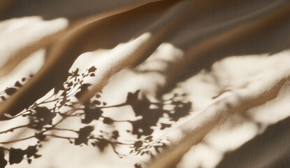 A close-up of a light beige linen fabric with a shadow of a leafy branch cast on the surface.