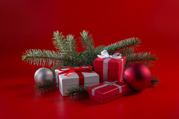 Gifts in boxes, fir branches and Christmas tree decorations on a red background