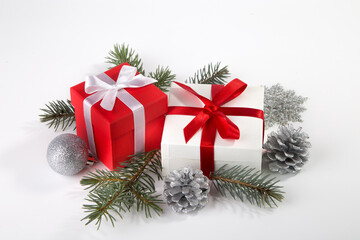 Two boxes with a gift tied with satin ribbons, a fir branch and Christmas tree decorations on a white background