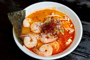 A bowl of  Ebi Japanese ramen noodles, featuring a soft egg, shrimp, and enoki mushroom in a spicy broth,