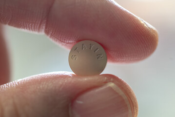 Fingers holding statin drug tablet - close-up 
