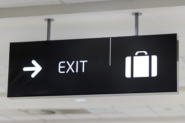 A sign indicating the direction to the exit hangs from the ceiling of the building