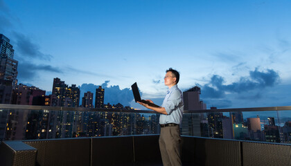 Young asian businessman with laptop on the building rooftop at city night