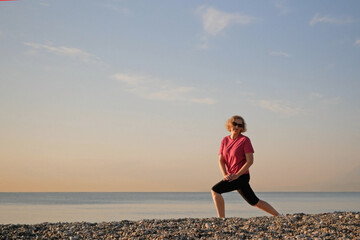 Middle aged woman doing yoga exercise on sea beach in the summer morning