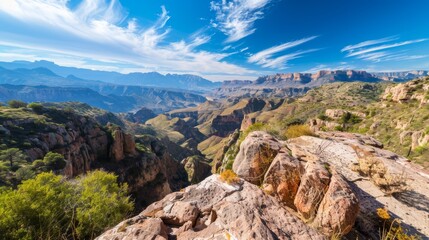 Obraz premium From a mountaintop, gaze down into a verdant valley dotted with rolling hills In the distance, majestic mountains rise, their peaks touching the clear, blue sky Scattered
