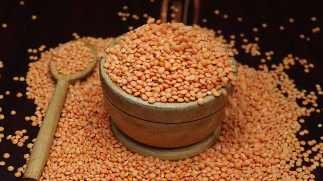Slow motion falling red lentils on a wooden bowl from top. Macro Shot Lentil Texture Pattern.  Vegetarian Healthy Food. Raw Organic Red Lentils Grains Fall in Slow Motion.
