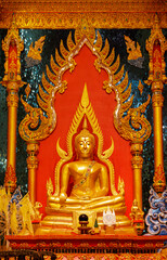 The golden Buddha image sits on a beautifully decorated Chukchi base. The Buddha image is enshrined inside a temple decorated with intricate patterns.