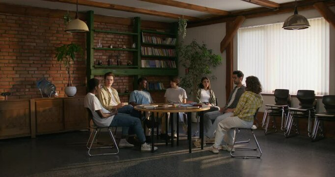 Bible Study Group. Young people are talking while sitting at a table indoors. Daylight
