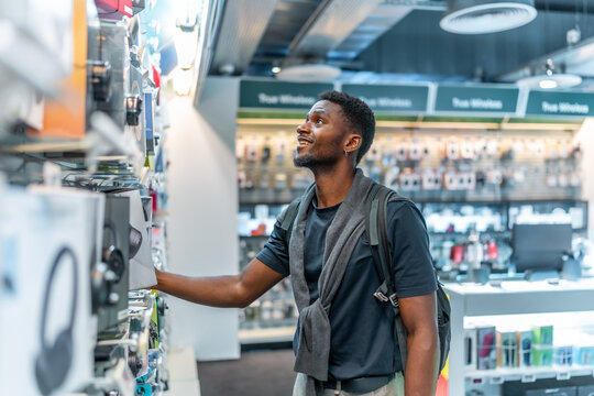 Young african man in a tech store looking at headphones - Powered by Adobe
