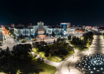 Aerial night Freedom Square panorama with fountain, University and hotel illuminated buildings in Kharkiv city center, Ukraine