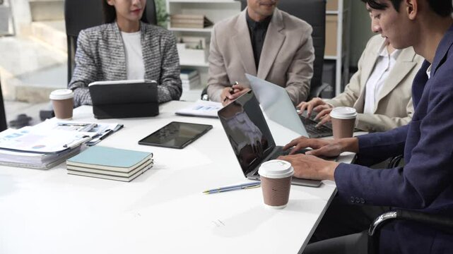 In an office, an Asian team meets at a desk, analyzing financial data on a monitor. They discuss business finance, operational guidelines, and strategies for success, data-driven decision-making.
