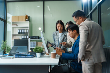 In an office, an Asian team meets at a desk, analyzing financial data on a monitor. They discuss business finance, operational guidelines, and strategies for success, data-driven decision-making.