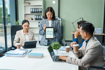In a boardroom, an Asian team meets at a desk, presenting financial terms and strategies. Executives and employees collaborate, sharing ideas and work guidelines for success during an annual meeting.
