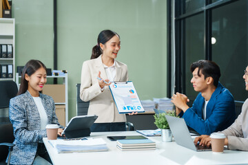 In a boardroom, an Asian team meets at a desk, presenting financial terms and strategies. Executives and employees collaborate, sharing ideas and work guidelines for success during an annual meeting.