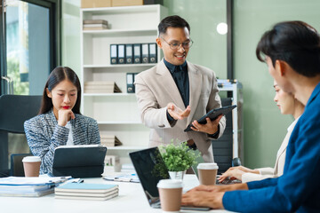 In a boardroom, an Asian team meets at a desk, presenting financial terms and strategies. Executives and employees collaborate, sharing ideas and work guidelines for success during an annual meeting.