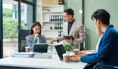 In a boardroom, an Asian team meets at a desk, presenting financial terms and strategies. Executives and employees collaborate, sharing ideas and work guidelines for success during an annual meeting.