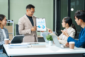 In a boardroom, an Asian team meets at a desk, presenting financial terms and strategies. Executives and employees collaborate, sharing ideas and work guidelines for success during an annual meeting.