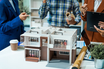 In an office room, architect-engineer team discusses modern house model at desk. They review...